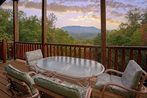 A wooden deck with a glass-top table and wicker chairs, overlooking a mountainous landscape. - Cabin w/Private Pool-Theater-Mountain View-Game Room (GATLINBURG)