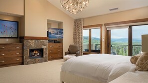 Un dormitorio con una cama grande, chimenea, televisor y balcón con vistas panorámicas.