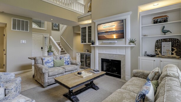 A spacious living room with a fireplace, a television mounted above it, and a staircase leading to an upper level. - 7634 Huntington-Canal views, heated pool & spa.  Quick walk to Ocean. (Hilton Head Island)