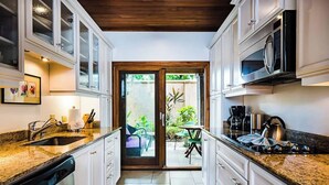 Cocina con alacenas blancas, encimera de granito, lavavajillas, estufa y microondas. Hay una puerta corrediza de vidrio que da a un patio con mesa y sillas.