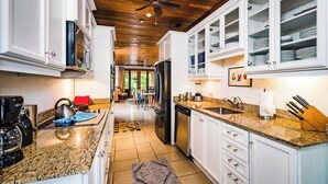 Una cocina moderna con encimeras de granito, armarios blancos y un ventilador de techo.