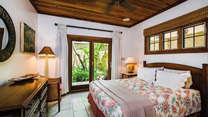 Un dormitorio con cama, escritorio, silla, lámpara y vista a zonas verdes a través de una puerta corredera.