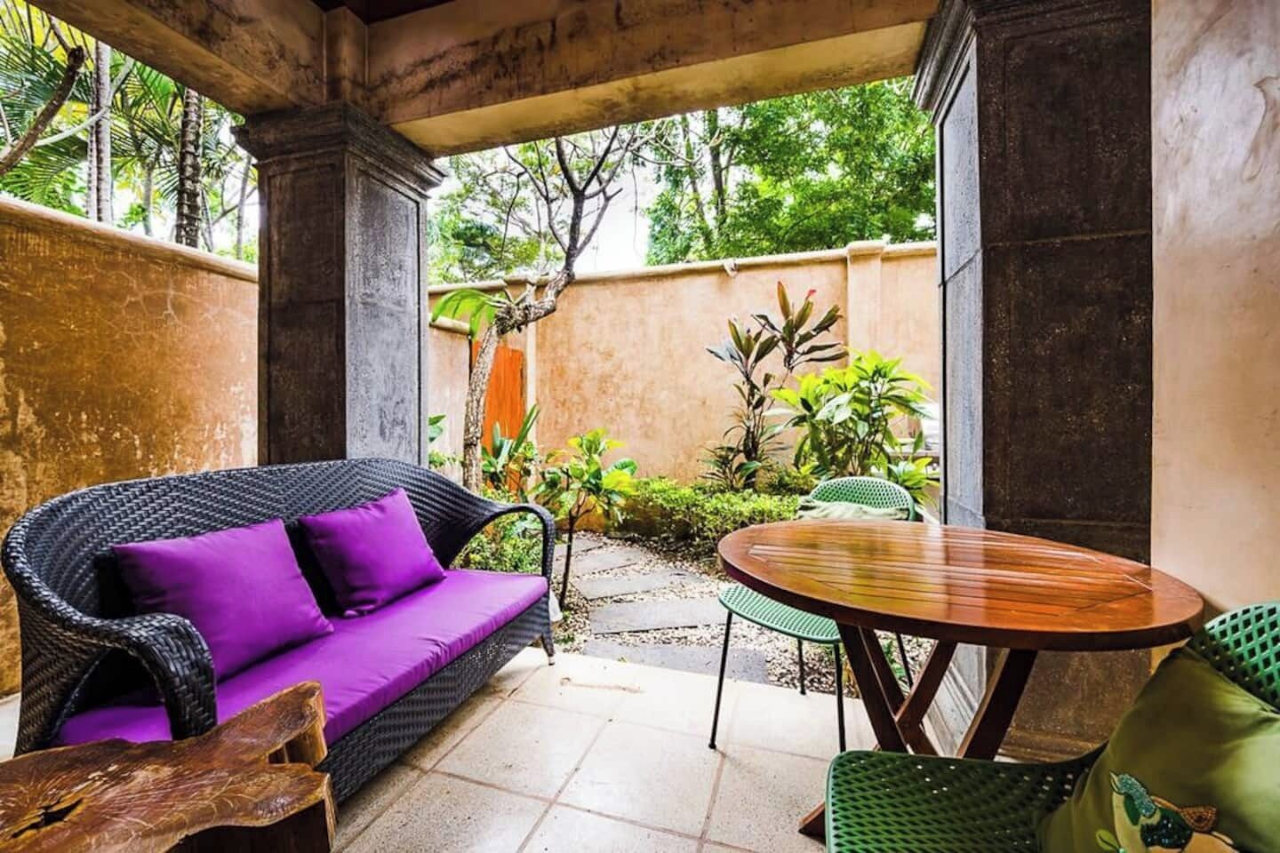 An outdoor patio area with a wicker sofa, a round wooden table, and chairs.