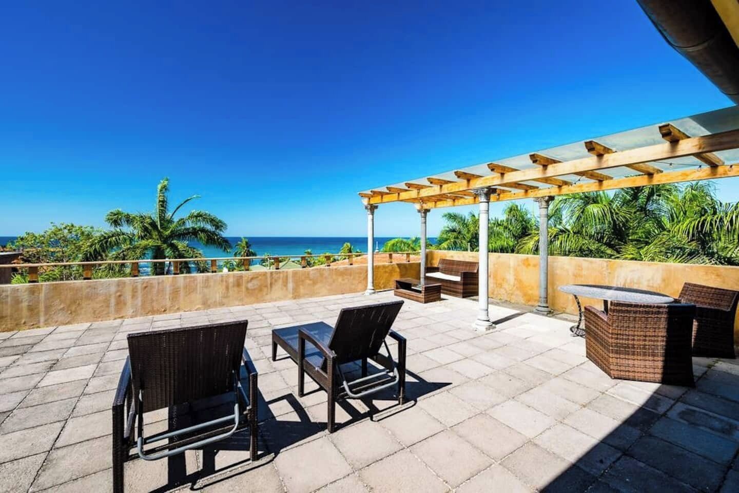 Una terraza en la azotea con mobiliario exterior, un pérgola y vistas al océano.