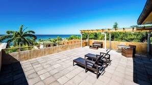 Una terraza en la azotea con vista al océano, mobiliario exterior y una pérgola.