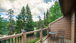 A wooden deck with a railing, two metal chairs, and a table.