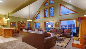A spacious living room with a large brown leather sofa, a dining area with wooden chairs and a table, and a kitchen with wooden cabinets and a hanging light fixture.