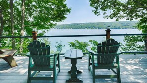 A deck with two Adirondack chairs and a small table, overlooking a lake with a forested shoreline.