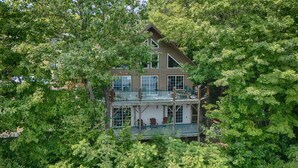 A two-story house with a balcony and large windows, surrounded by dense trees.
