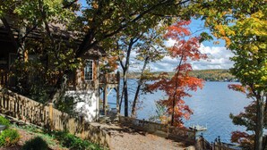 A lakeside cabin with a wooden deck and a stone wall.