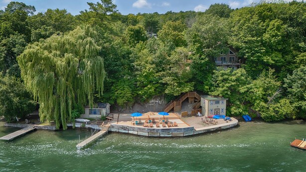 A lakeside property with a dock, a small wooden structure with a deck, and lush greenery.