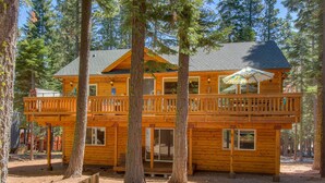 A two-story wooden cabin with a balcony on the upper floor, surrounded by trees.