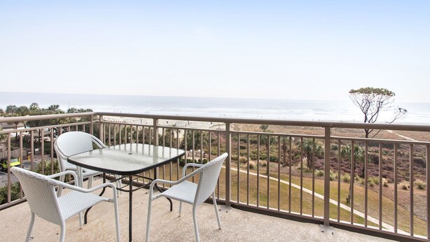 Un balcón con mesa y sillas, con vista a una playa y al océano.