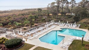 Zona de piscina con múltiples tumbonas y sombrillas, rodeada de jardines ajardinados y vista al océano.