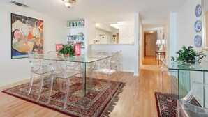 Un comedor moderno con una mesa y sillas de vidrio, rodeado de estanterías y una cocina al fondo.
