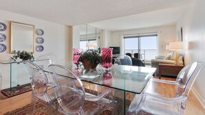 Un salón moderno con una mesa de comedor de vidrio, sillas de plástico transparente, un sofá y un balcón con vistas.