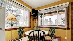 Un comedor con una mesa redonda y cuatro sillas, una lámpara y un televisor montado en la pared.