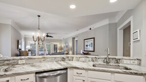 A modern kitchen with white cabinetry, a marble countertop, and a dishwasher.
