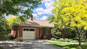 A single-story brick house with a garage, surrounded by a well-maintained lawn and trees. - Peaceful Boise Bungalow, Short Drive to Downtown! (Boise)