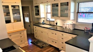 A kitchen with white cabinets, a black countertop, and a window with blinds. - Peaceful Boise Bungalow, Short Drive to Downtown! (Boise)