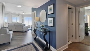 Uma sala de estar moderna com uma parede azul de destaque, um espelho redondo grande e um aparador com um vaso de flores.