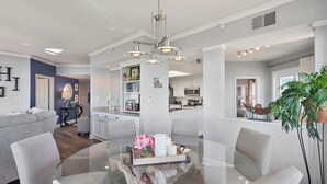 Uma sala de estar moderna com uma mesa de centro de vidro, sofás cinzas e uma área de jantar com mesa e cadeiras de vidro.