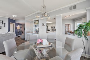 A modern living room with a glass coffee table, grey sofas, and a dining area with a glass table and chairs. - 4th floor oceanfront, end unit in Palmetto Dunes! Ocean views from each room! (Hilton Head Island)