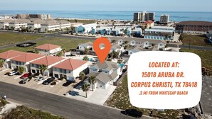 An aerial view of Corpus Christi, Texas, highlighting a residential area with multiple-story buildings, a clear view of the ocean, and a road leading to the beach. - Remodeled Coastal Retreat | Heated Pool, Private Patio & King Beds (Corpus Christi)