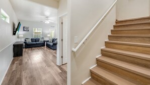 A modern interior with a wooden staircase, a living room with a dark-colored sofa, and a hallway leading to another room. - Remodeled Coastal Retreat | Heated Pool, Private Patio & King Beds (Corpus Christi)