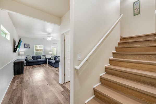 A modern interior with a wooden staircase, a living room with a dark-colored sofa, and a hallway leading to another room.
