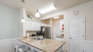 A modern kitchen with white cabinets, a granite countertop, and a stainless steel refrigerator. - Remodeled Coastal Retreat | Heated Pool, Private Patio & King Beds (Corpus Christi)