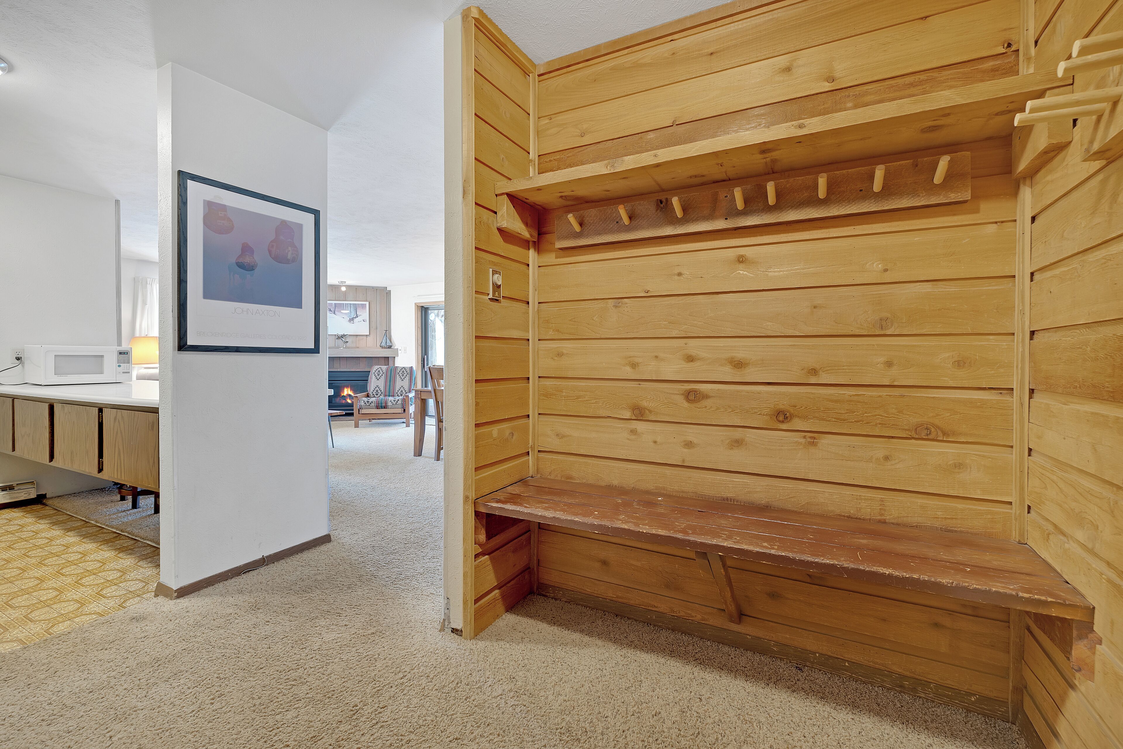 A room with a wooden bench, a white wall, and a framed picture.
