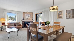 A dining area with a wooden table, chairs, and a bench. There is a fireplace, a sofa, and a lamp. - Affordable Ski Condo with Rustic Charm: Ski-In Access, Close to Main St dba12 (Breckenridge)