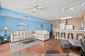 A modern living room with a sectional sofa, a coffee table, and a dining area with bar stools.
