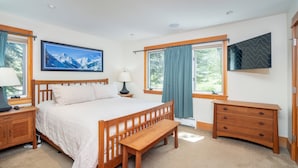 Une chambre à coucher avec un lit en bois, un banc, une table de chevet, une commode et une grande fenêtre avec des rideaux.