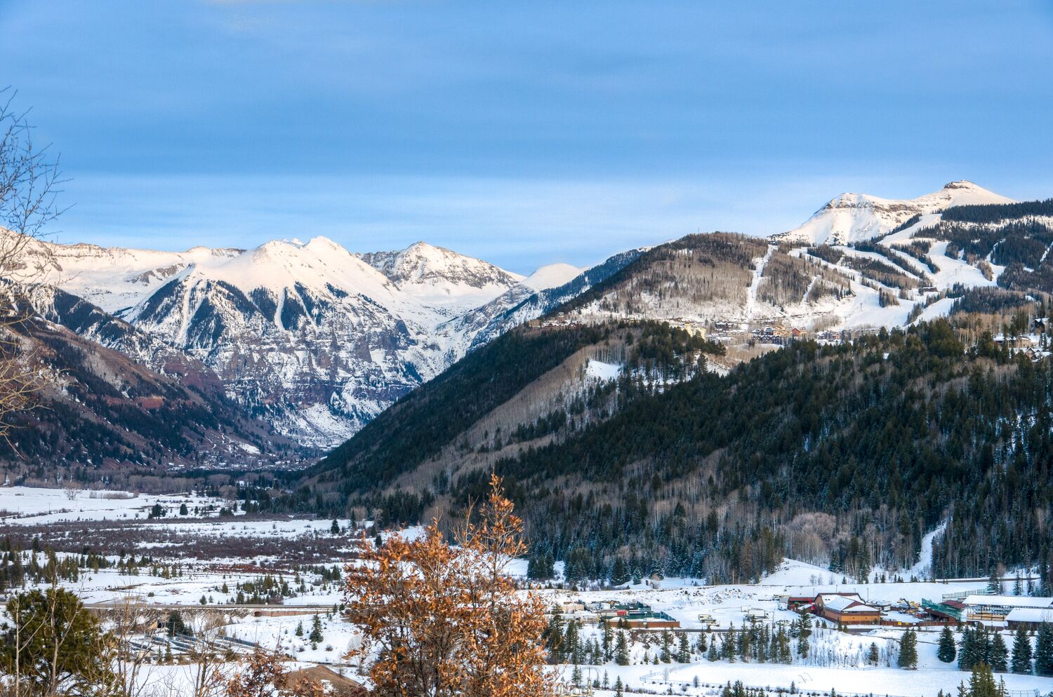 Paesaggio montuoso con cime innevate e una valle con edifici.
