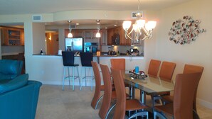 A modern kitchen with a dining area, featuring a glass-top table, brown chairs, and a chandelier. - Direct Ocean 3 bed, 3 1/2 bath (Cocoa Beach)