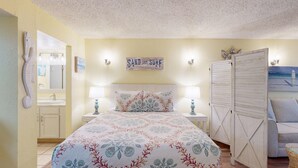 Quarto com cama, duas mesas de cabeceira, um criado-mudo, espelho, obra de arte na parede e guarda-roupa.