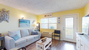 A living room with a couch, coffee table, and a 'BEACH' sign on the wall.