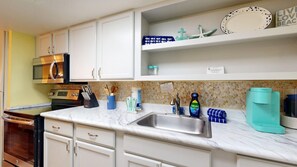 A kitchen with white cabinets, a stainless steel sink, a microwave, and a coffee maker. - Studio Condo in Town, Near Beach, Shared Pool and Hot Tub (Port Aransas)
