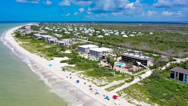 An aerial view of a coastal resort with beachfront villas, a sandy beach, and lush greenery.