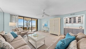 A spacious living room with a large window, a ceiling fan, and a view of the beach.