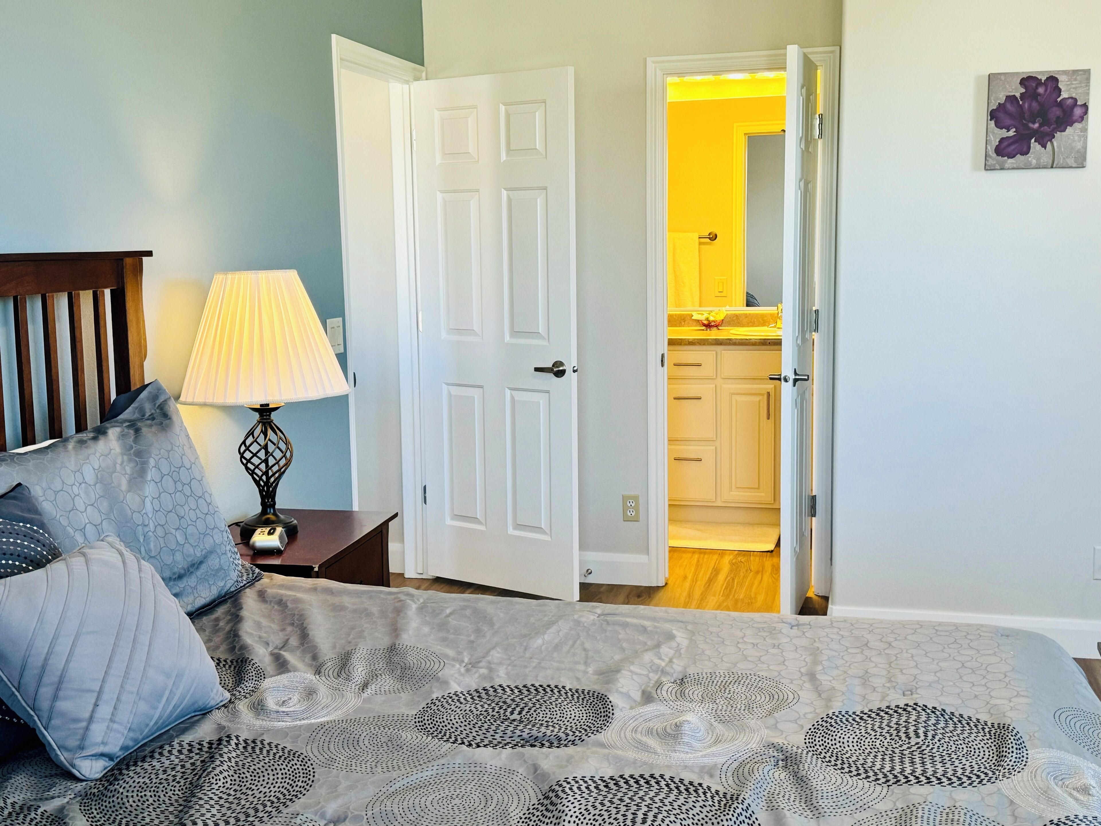 Une chambre à coucher avec un lit, une table de chevet avec une lampe et une porte donnant sur une salle de bain.