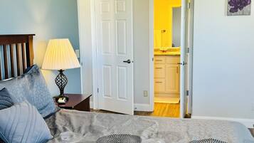 Une chambre à coucher avec un lit, une table de chevet avec une lampe et une porte donnant sur une salle de bain.