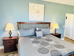 Un dormitorio con cama, dos mesitas de noche, cabecero de madera y una obra de arte colgada en la pared.