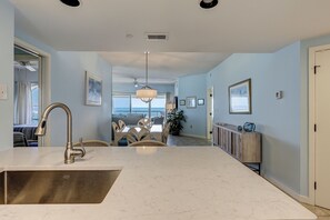 A modern kitchen with a large island, a dining area with a view, and a living space with a ceiling fan.