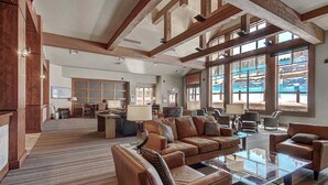 A spacious living area with a large sofa set, a coffee table, and a fireplace. There are multiple windows providing natural light and a view of the outdoors.