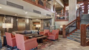 A spacious lobby with a high ceiling, a fireplace, comfortable seating, and a staircase leading to an upper level.