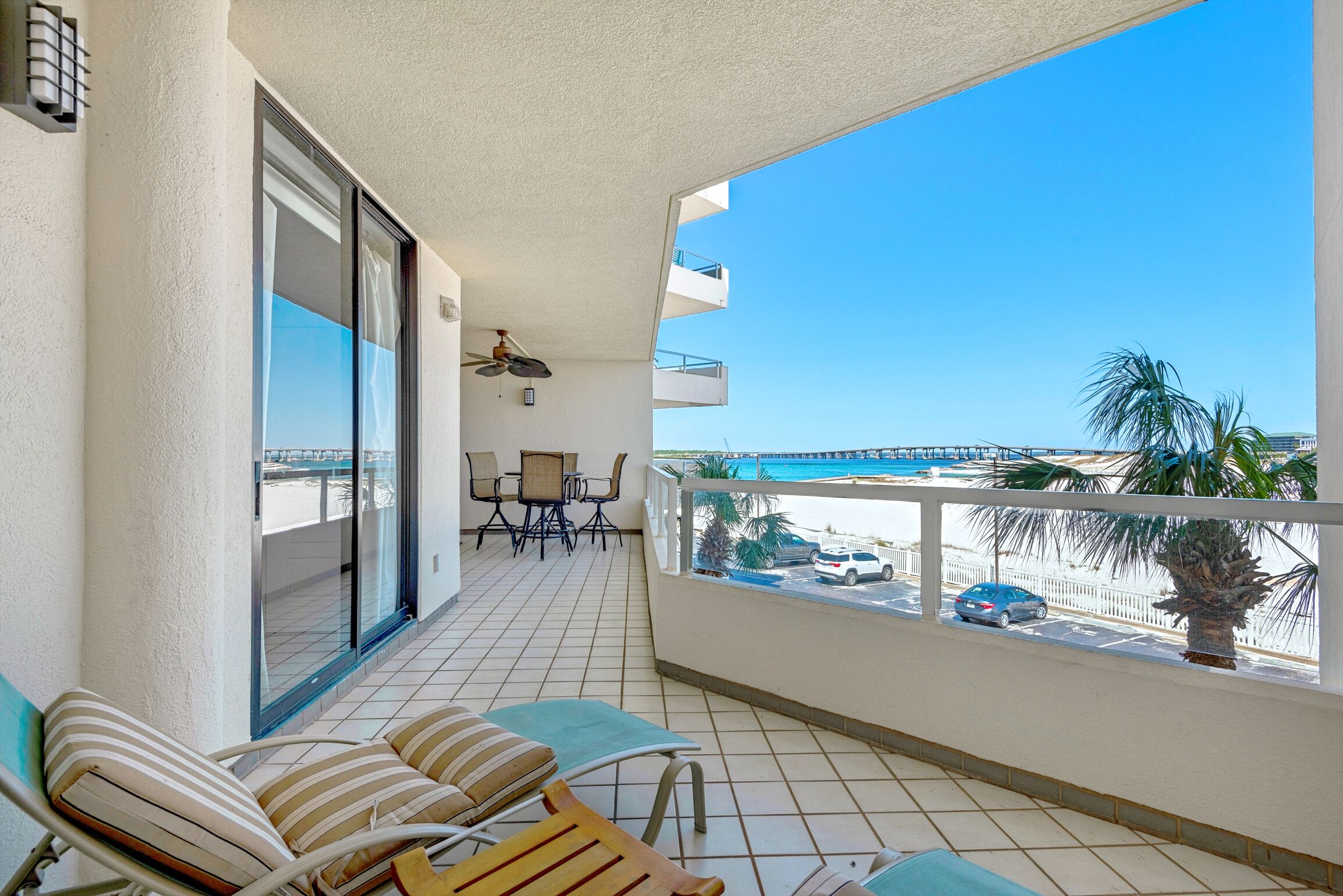 A balcony with a view of the ocean, a table with chairs, and a ceiling fan.