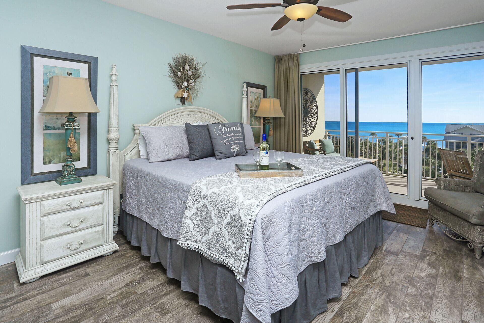 A bedroom with a large bed, two bedside tables, a dresser, and a view of the ocean through a sliding glass door.